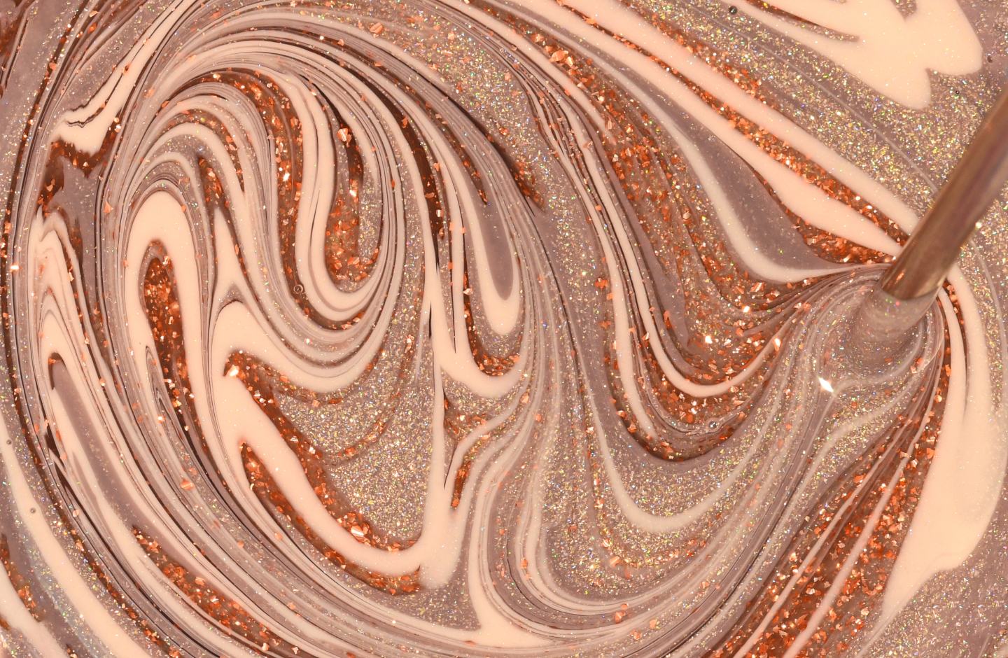 Swirls of pink, copper, and silver glitter being blended into nail polish