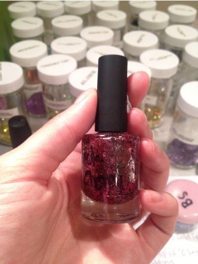 A handmade red-glitter nail polish held in front of jars of mixing supplies