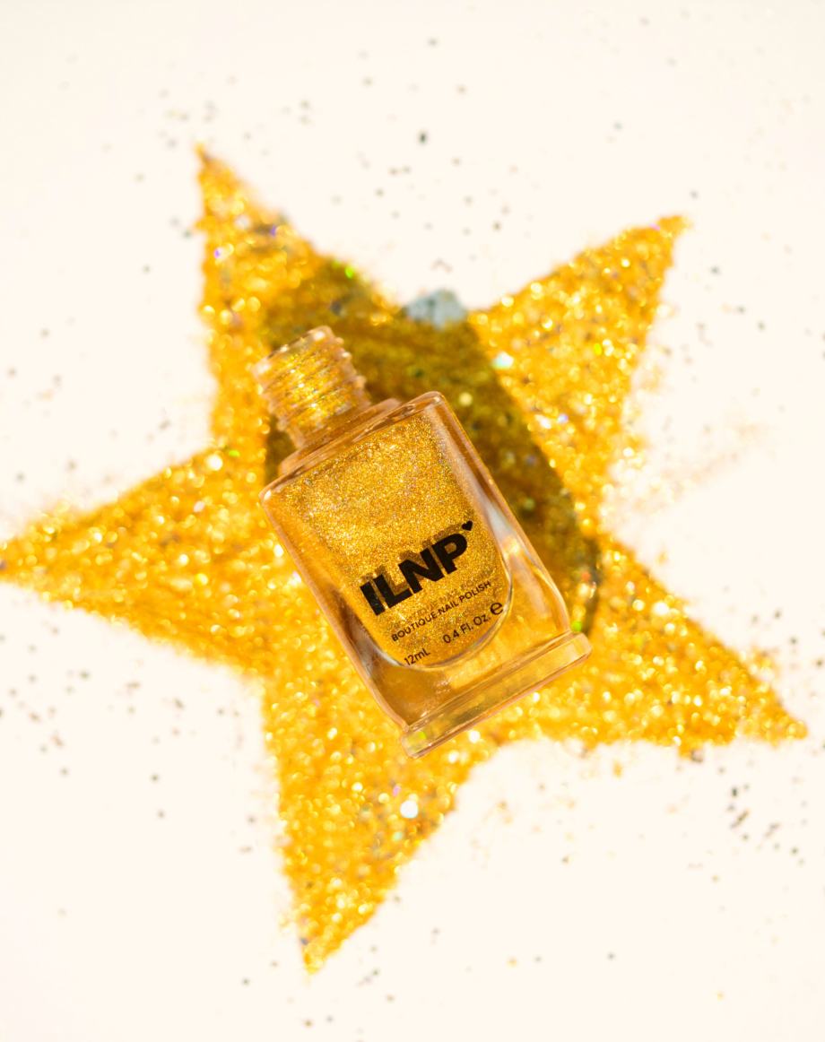 An ILNP gold-glitter polish bottle resting on a star drawn in gold glitter