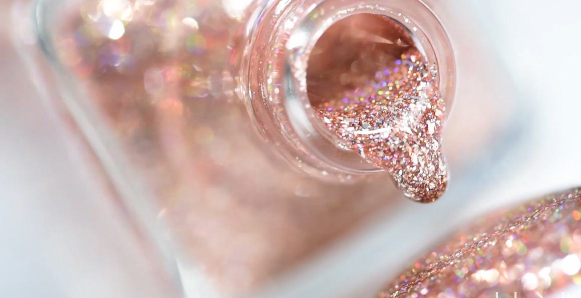 Close-up of rose-gold glitter nail polish dripping from the neck of a bottle
