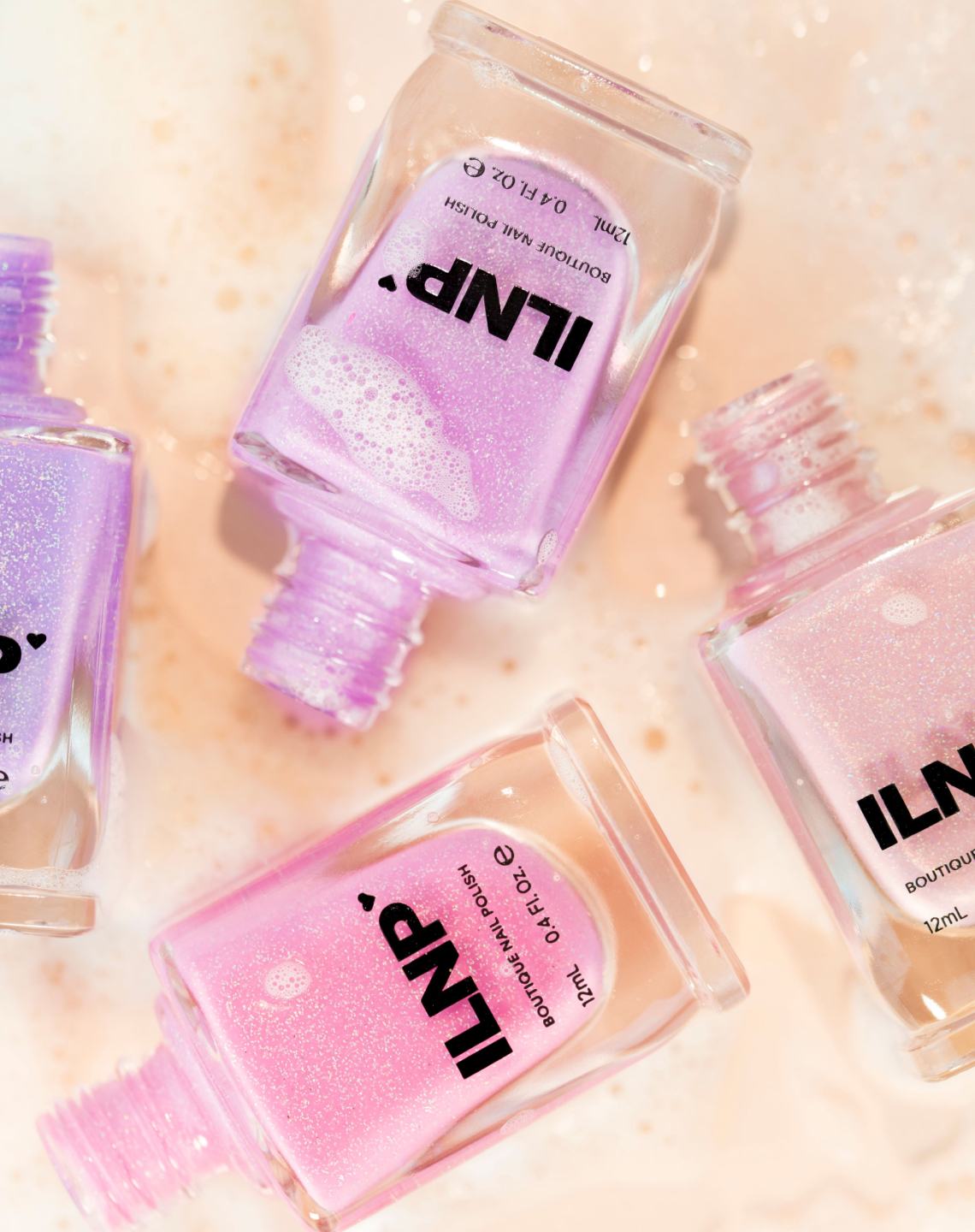 ILNP nail polish bottles in pink and lavender shades on a soapy surface