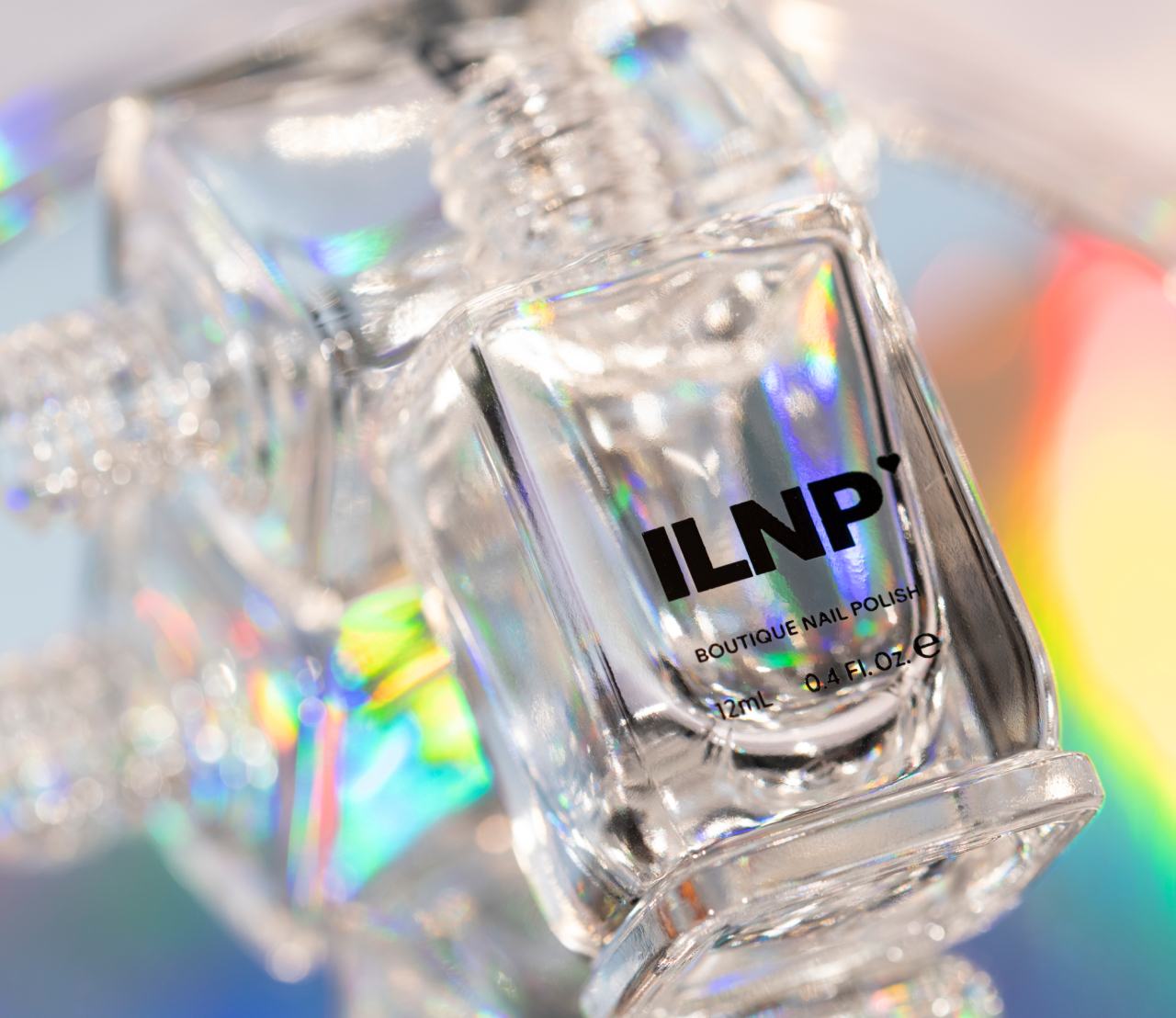 Close-up of a clear ILNP nail polish bottle catching rainbow holographic light